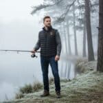 Lifestyle image of a man fishing outdoors wearing a Magnetar heated vest, quilted design for warmth during cold and misty weather.